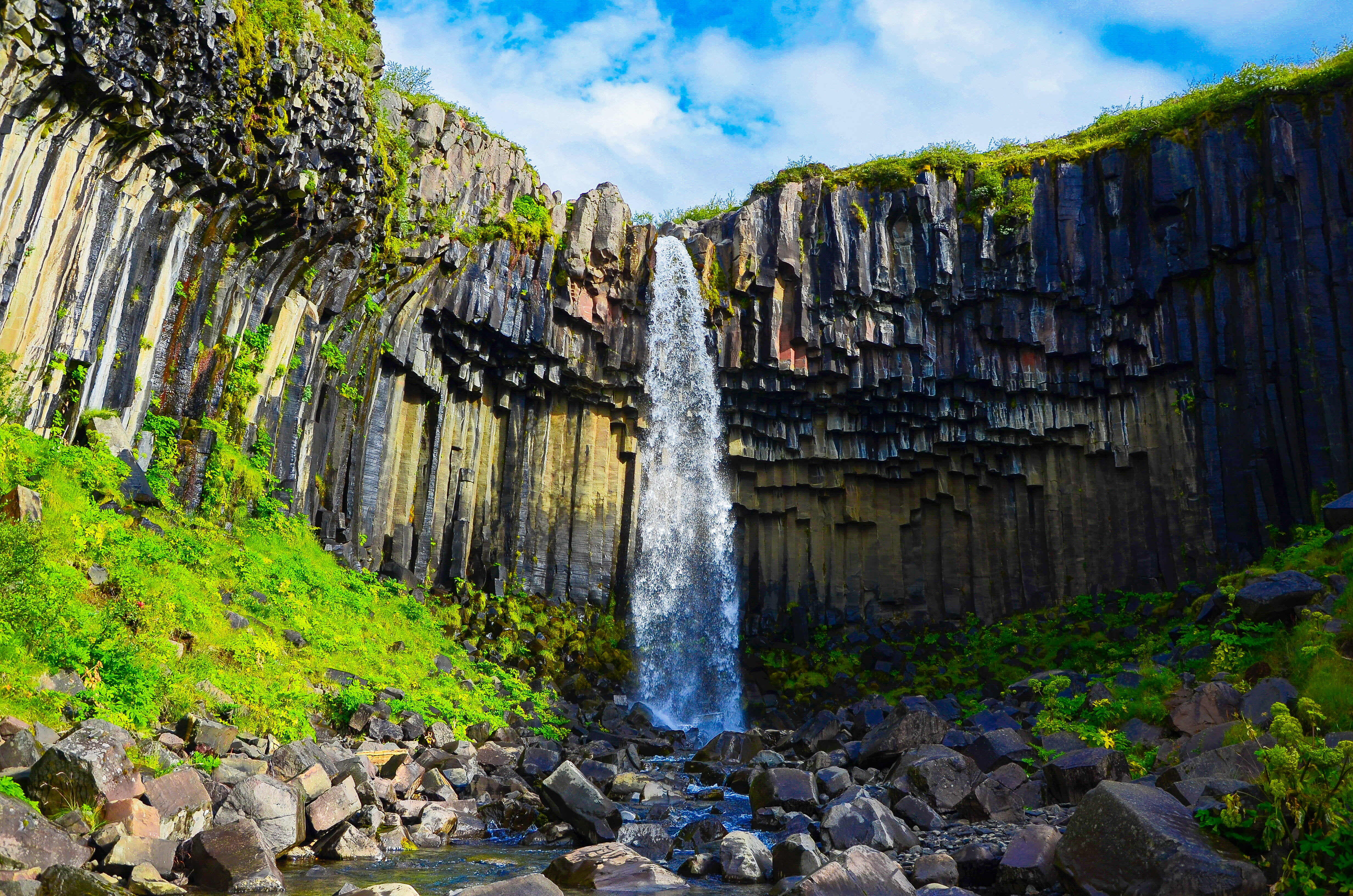 landscape photography of water falls surrounded by green plants under by cirrus clouds