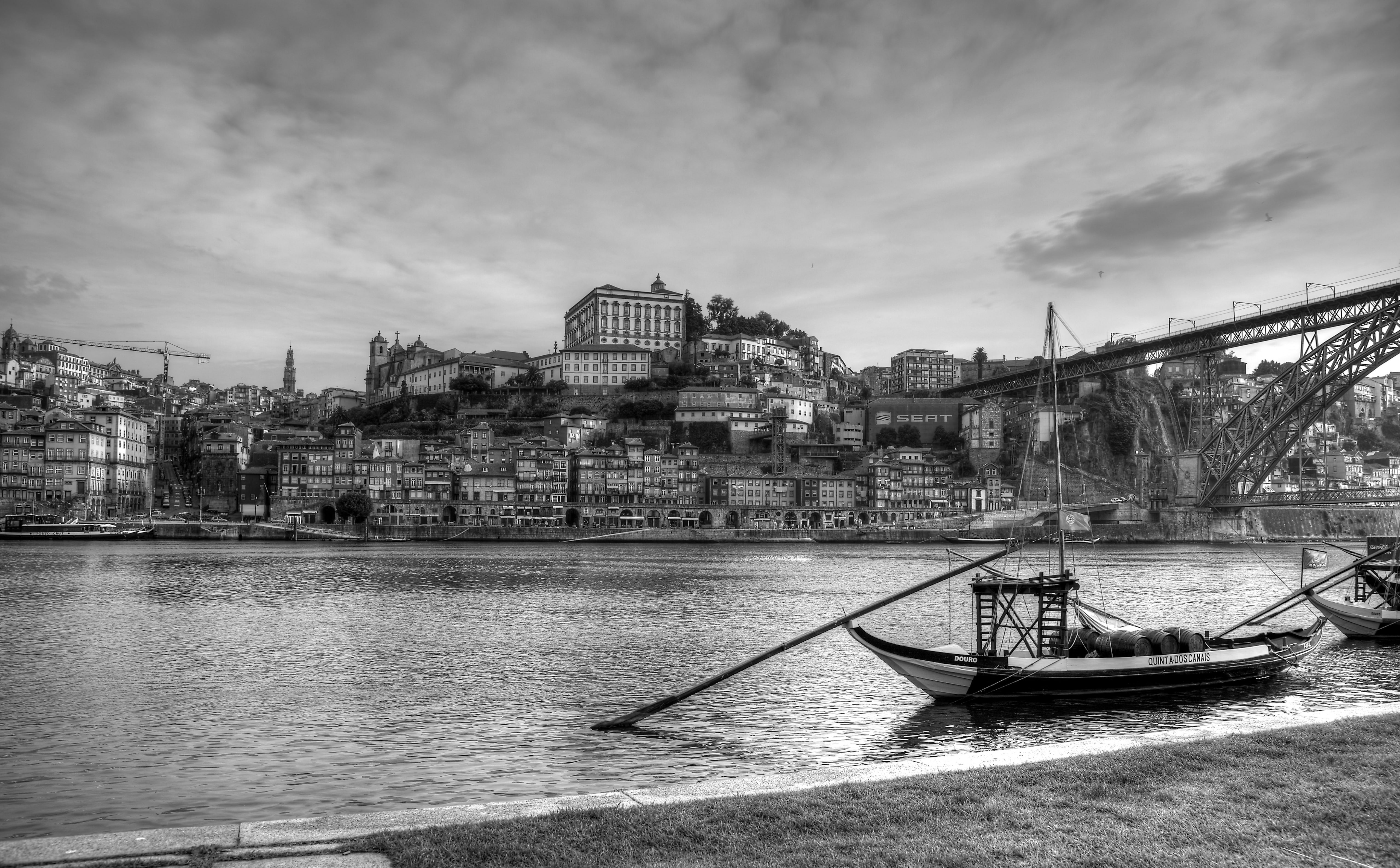 Cidade Invicta, grayscale photo of boat near bridge and village across body of water
