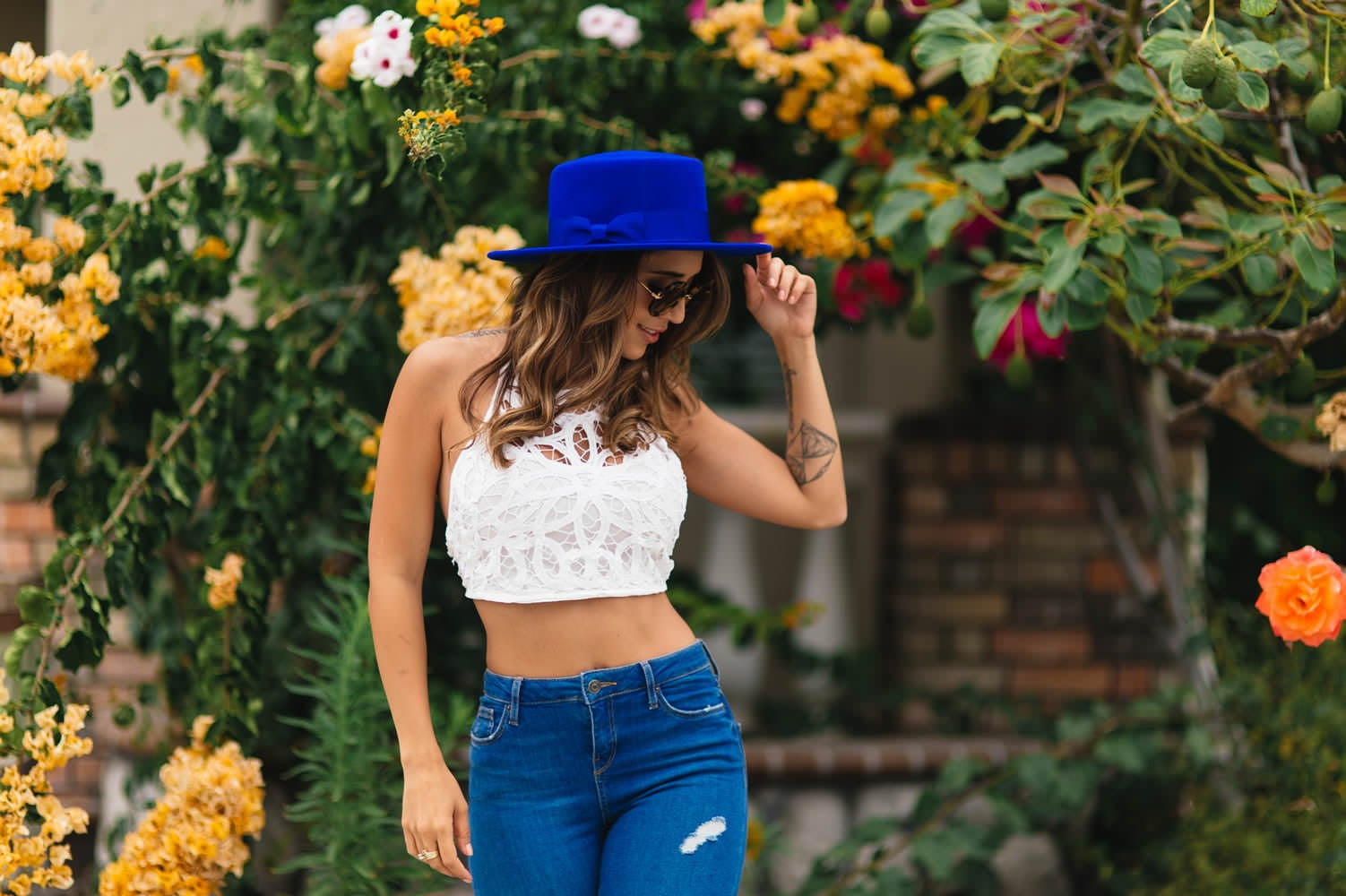 woman in white crop top and blue denim bottoms standing near flowers