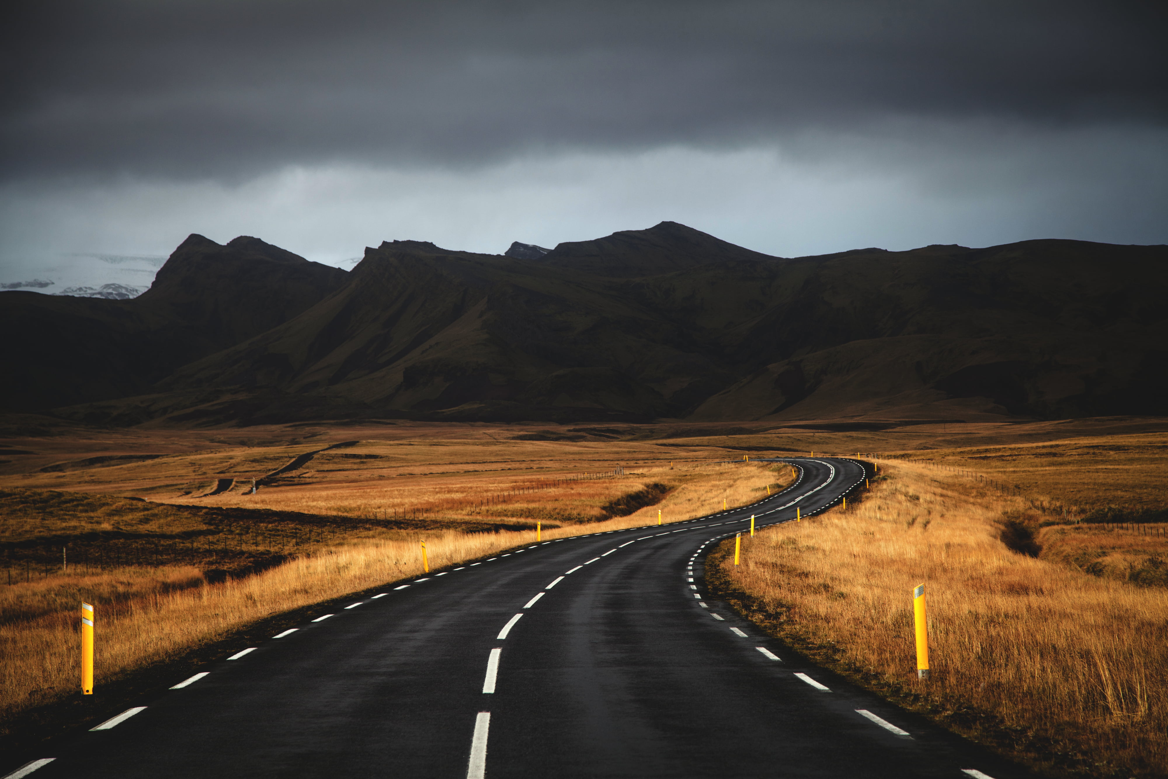 black concrete road near brown grass under cloudy sky, iceland