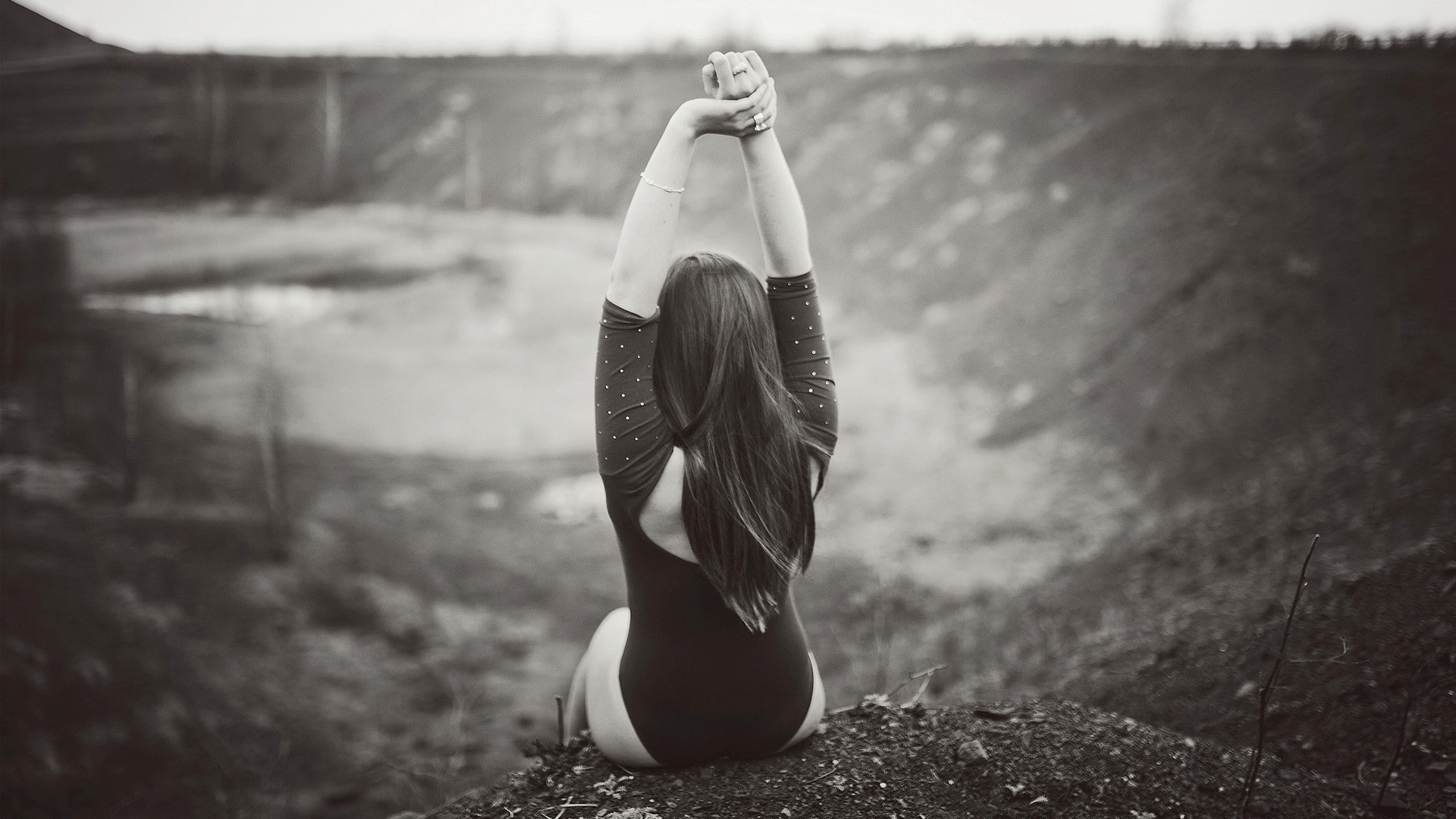 woman sitting on dirt with both hands on the air in grayscale photography