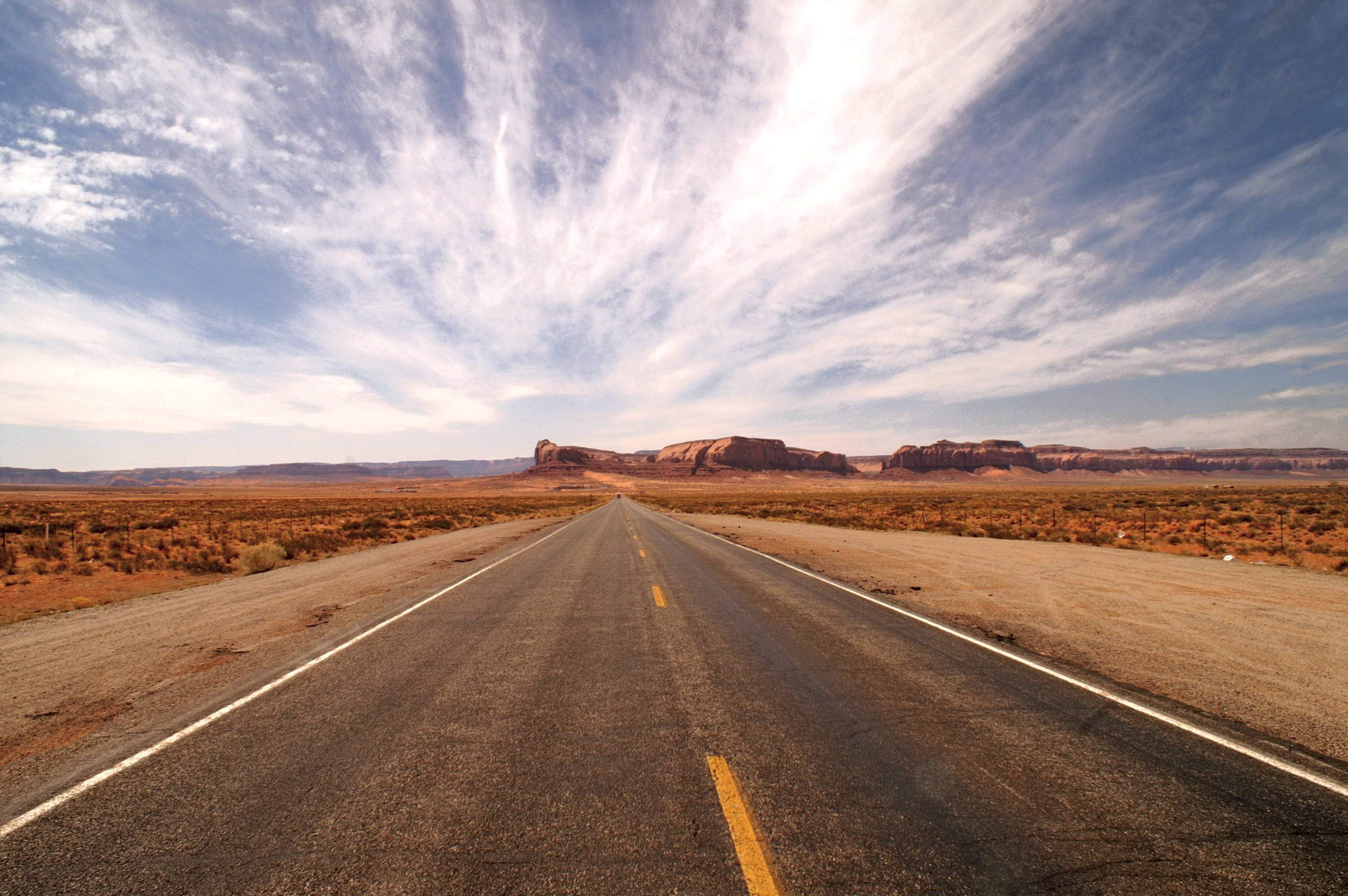 asphalt road in the middle of the desert under white clouds and blue sky during daytime