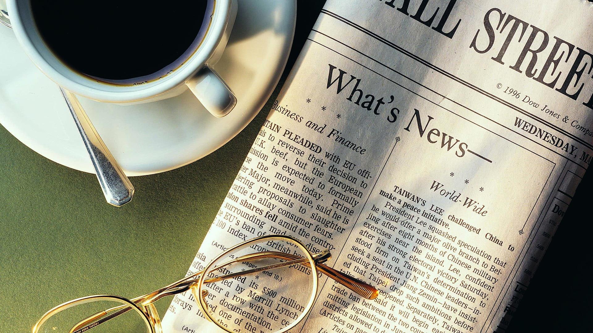 Coffee cup next to morning paper, news paper article and brass frame eyeglass