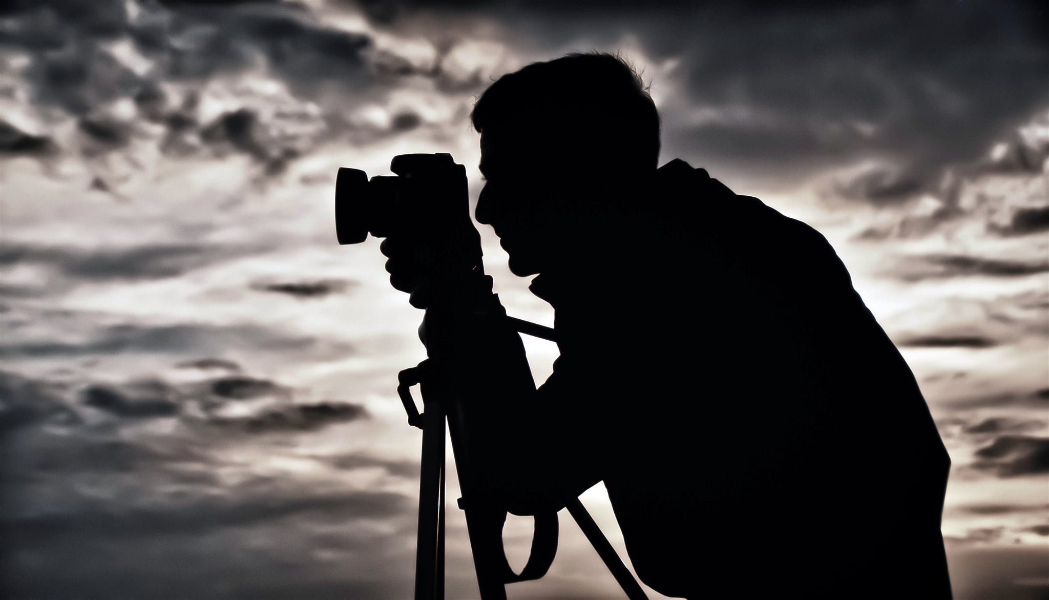 silhouette photography of man holding camera with tripod stand