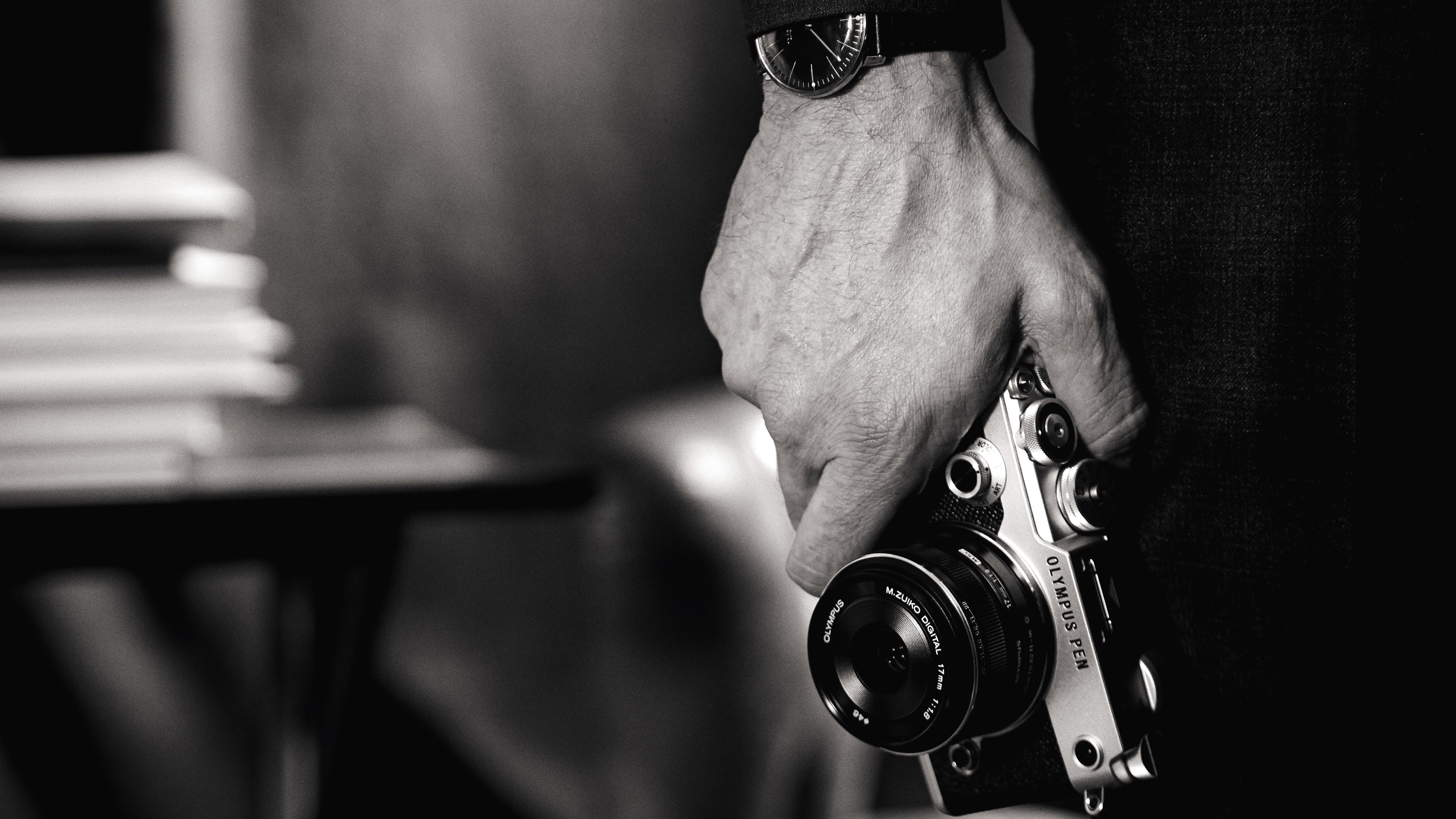 grayscale photo of man holding camera, Olympus PEN-F, mirrorless camera