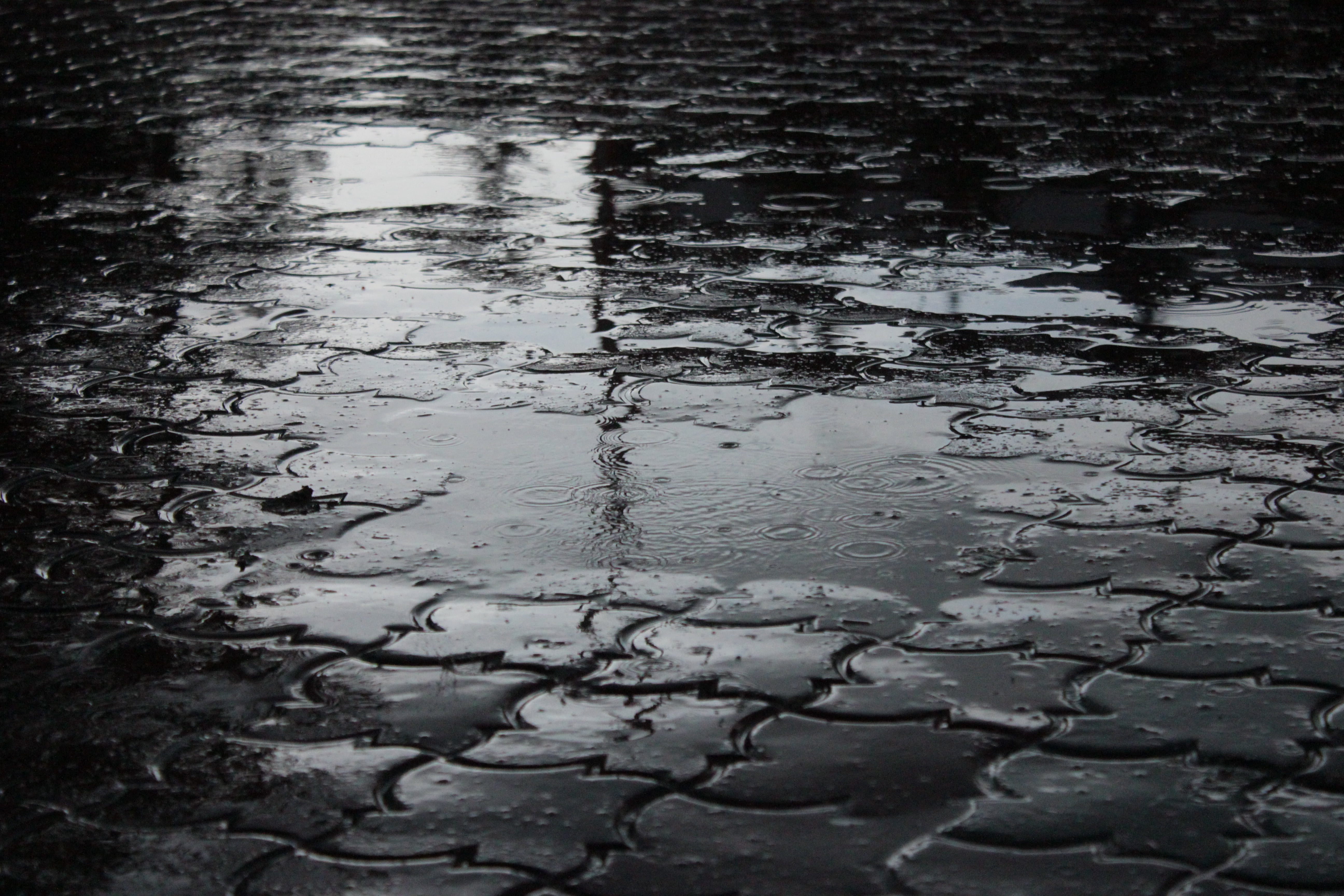 grayscale photo of raindrops on concrete floor, puddle, dark