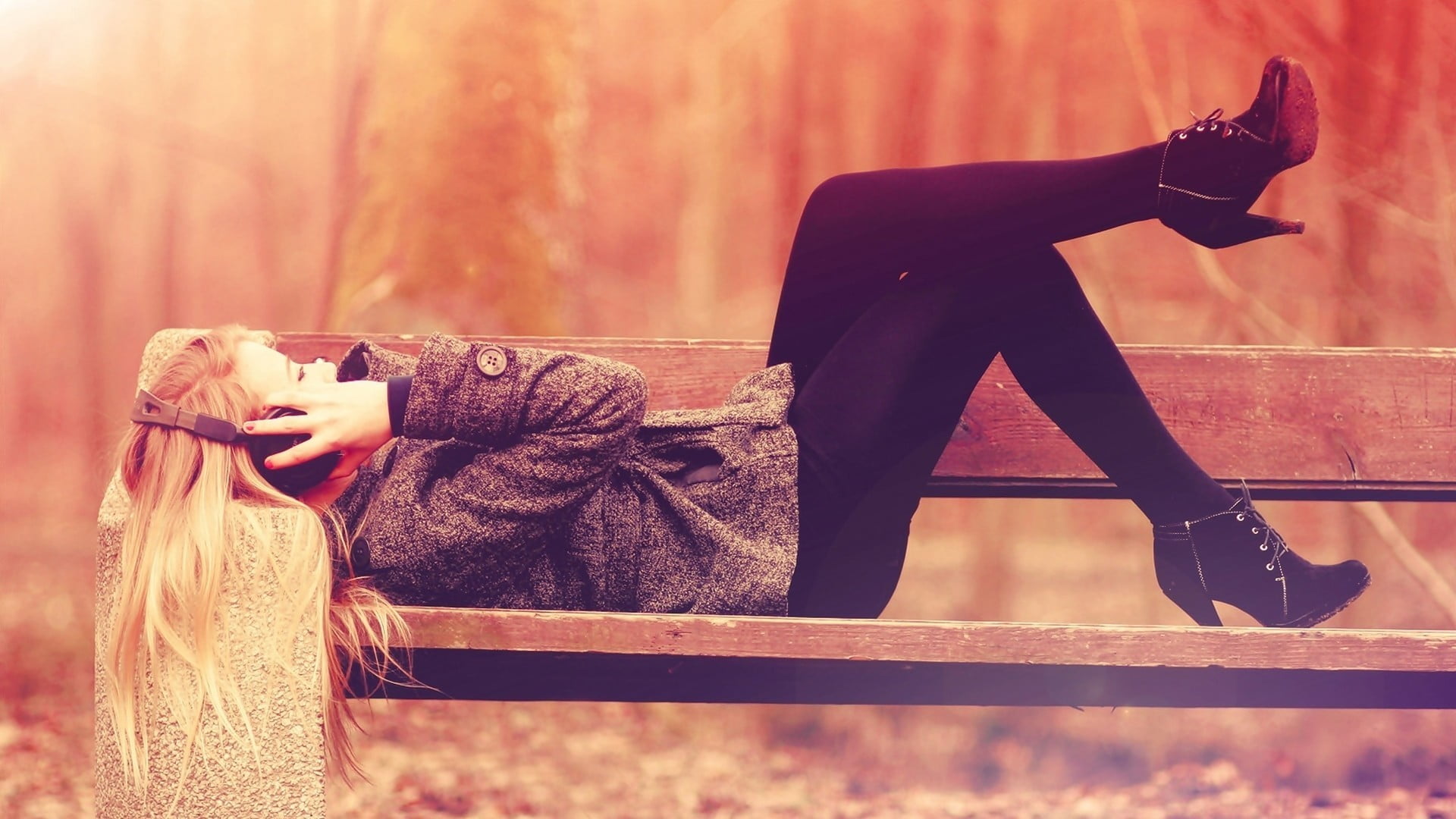 woman lying on brown bench holding headphones, blonde, music