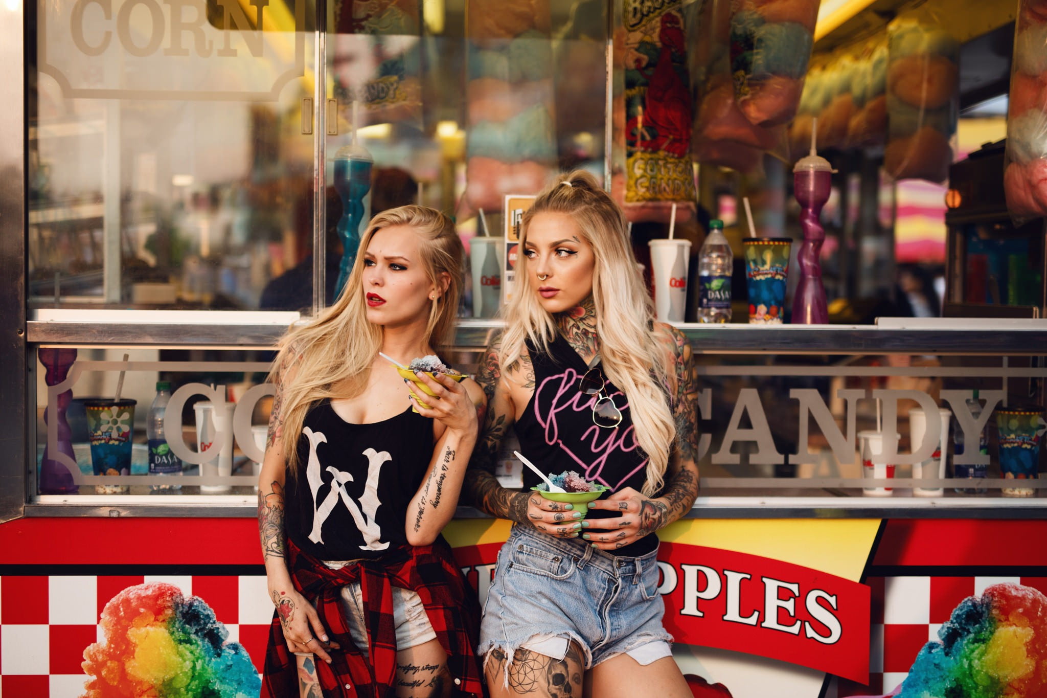 two women standing near storefront, blonde, tattoo, looking away